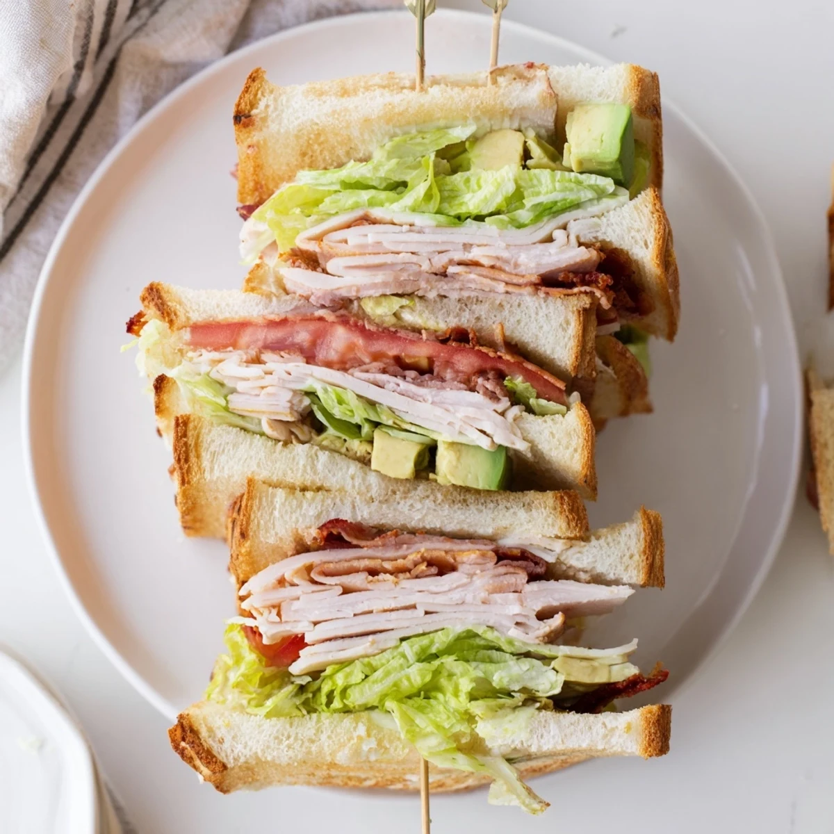 Toasted California Club Sandwich cut diagonally revealing layers of crispy bacon, fresh vegetables, and creamy mayonnaise