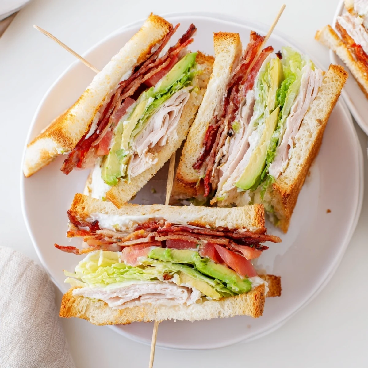 Hearty California Club Sandwich on white bread featuring turkey, bacon, avocado slices, and crisp lettuce