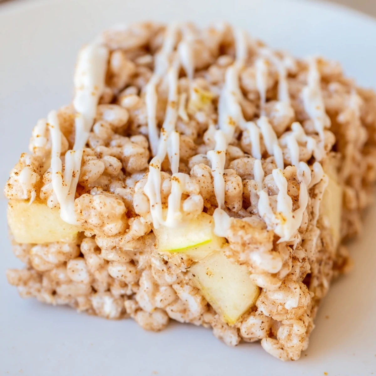 Square of Apple Pie Rice Krispie Treats topped with white chocolate drizzle on white plate