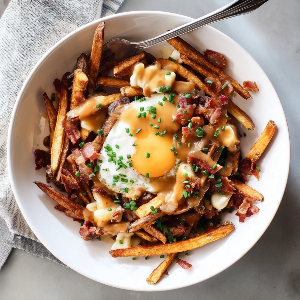 Golden crispy breakfast poutine topped with melted cheese curds, smoky bacon, and perfectly cooked eggs