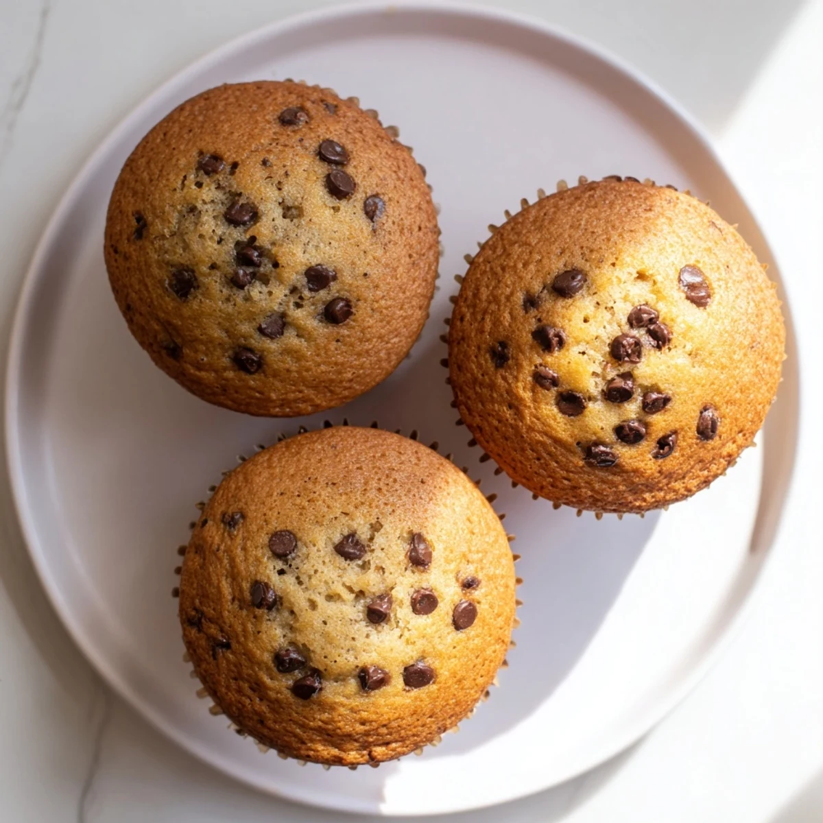 Golden brown banana chocolate chip muffins with melted chocolate tops on a wire rack