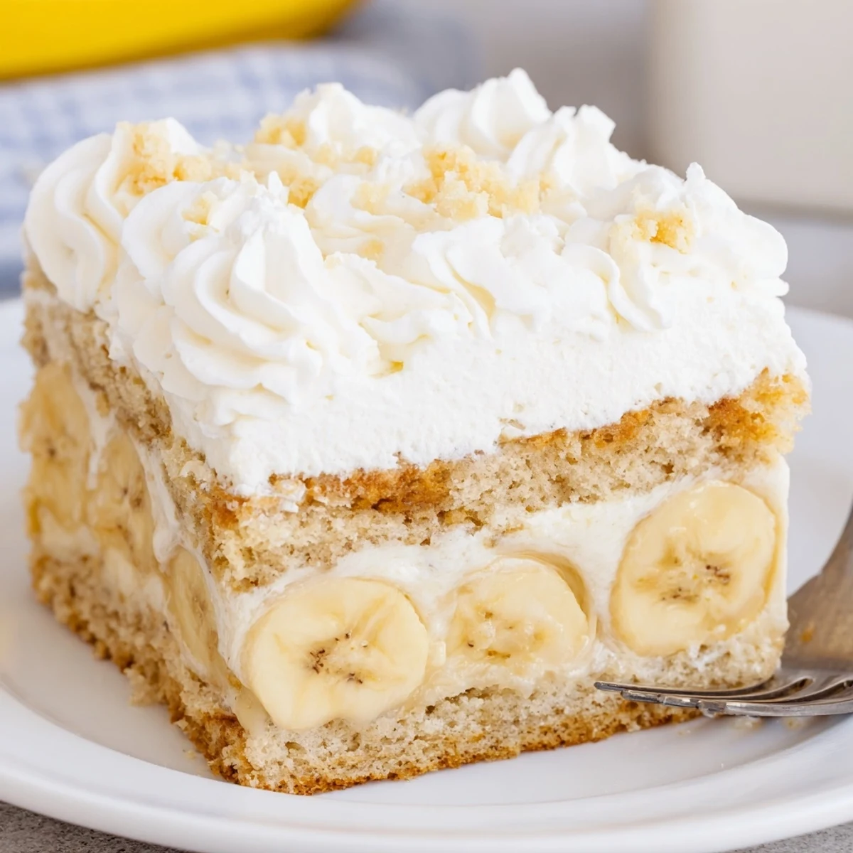 Banana Pudding Cake Recipe topped with whipped cream, crushed wafers, sliced bananas.  