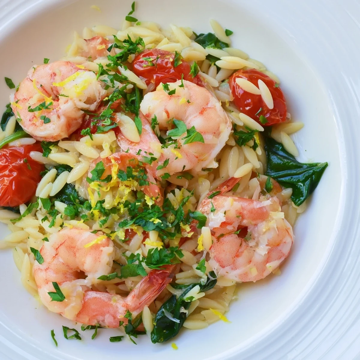 Golden seared shrimp nestled among lemon-infused orzo with wilted spinach and cherry tomatoes in a deep skillet
