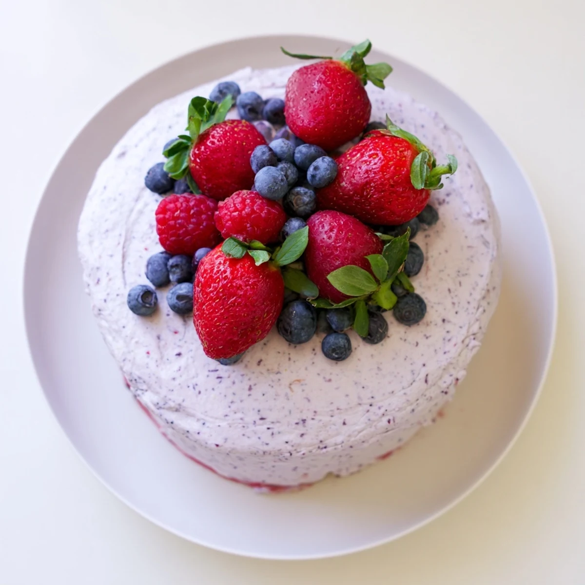 Homemade basil berry cake decorated with swirls of pink basil frosting and scattered blueberries