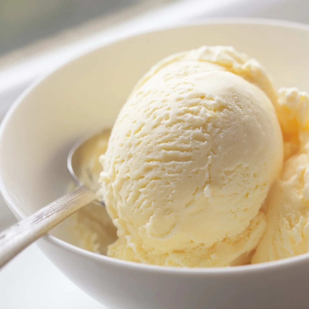 Creamy vanilla ice cream recipe served in a chilled glass bowl with a shiny silver scoop