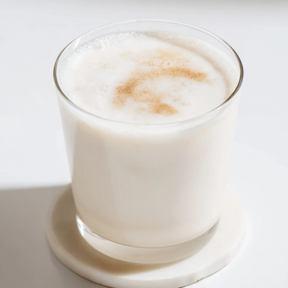 Fresh homemade almond milk poured into a clear glass jug showcasing its smooth creamy texture