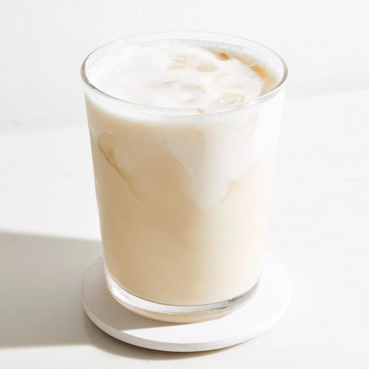 Glass of chilled homemade almond milk on wooden table with filtered sunlight and whole almonds nearby