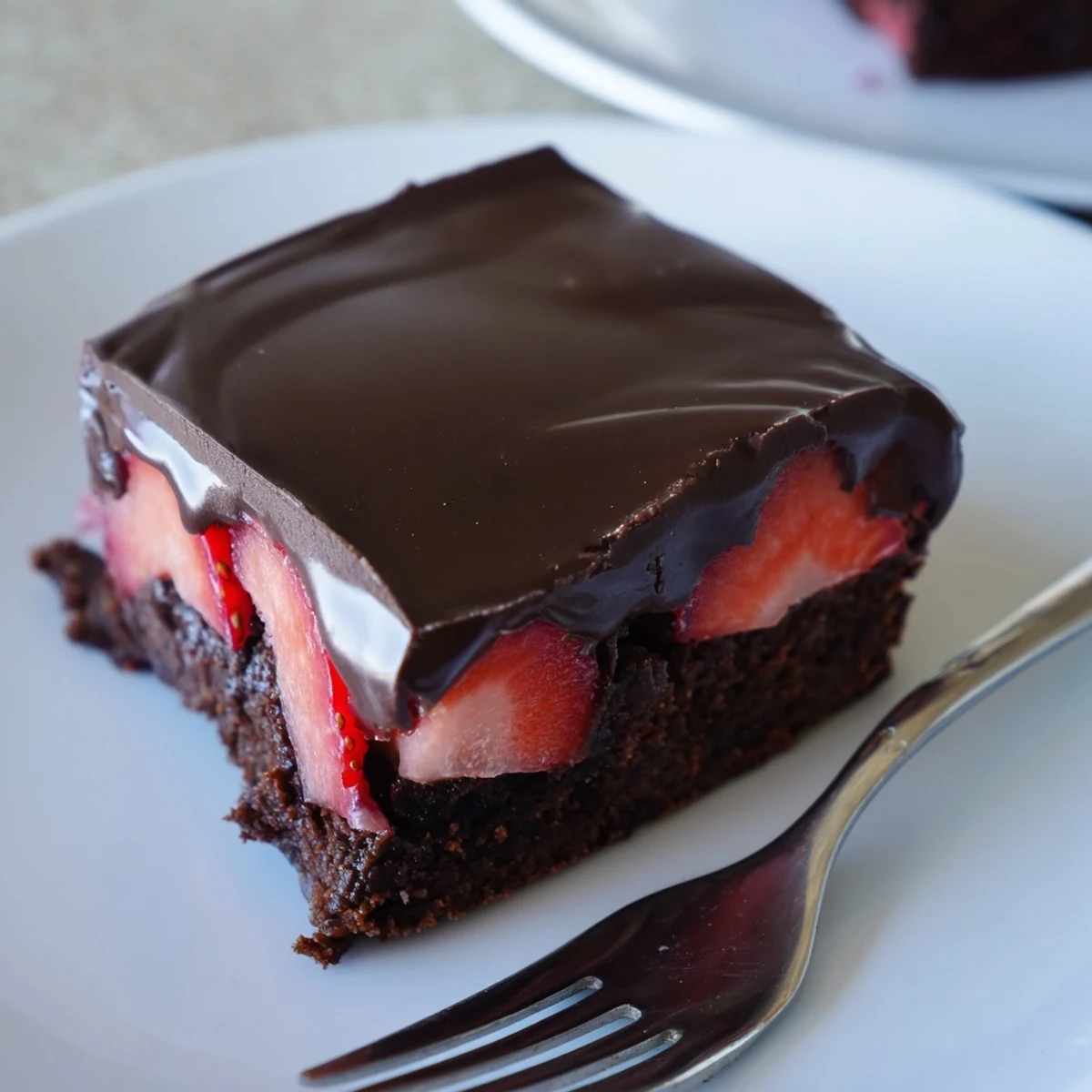 Dark chocolate covered strawberry brownies topped with a shiny ganache coating and fresh fruit
