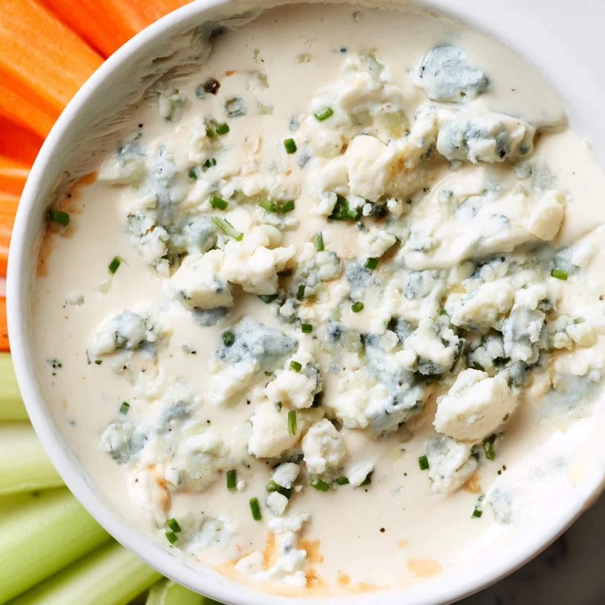 Velvety blue cheese dip with visible crumbles, scooped up by a crunchy pita chip