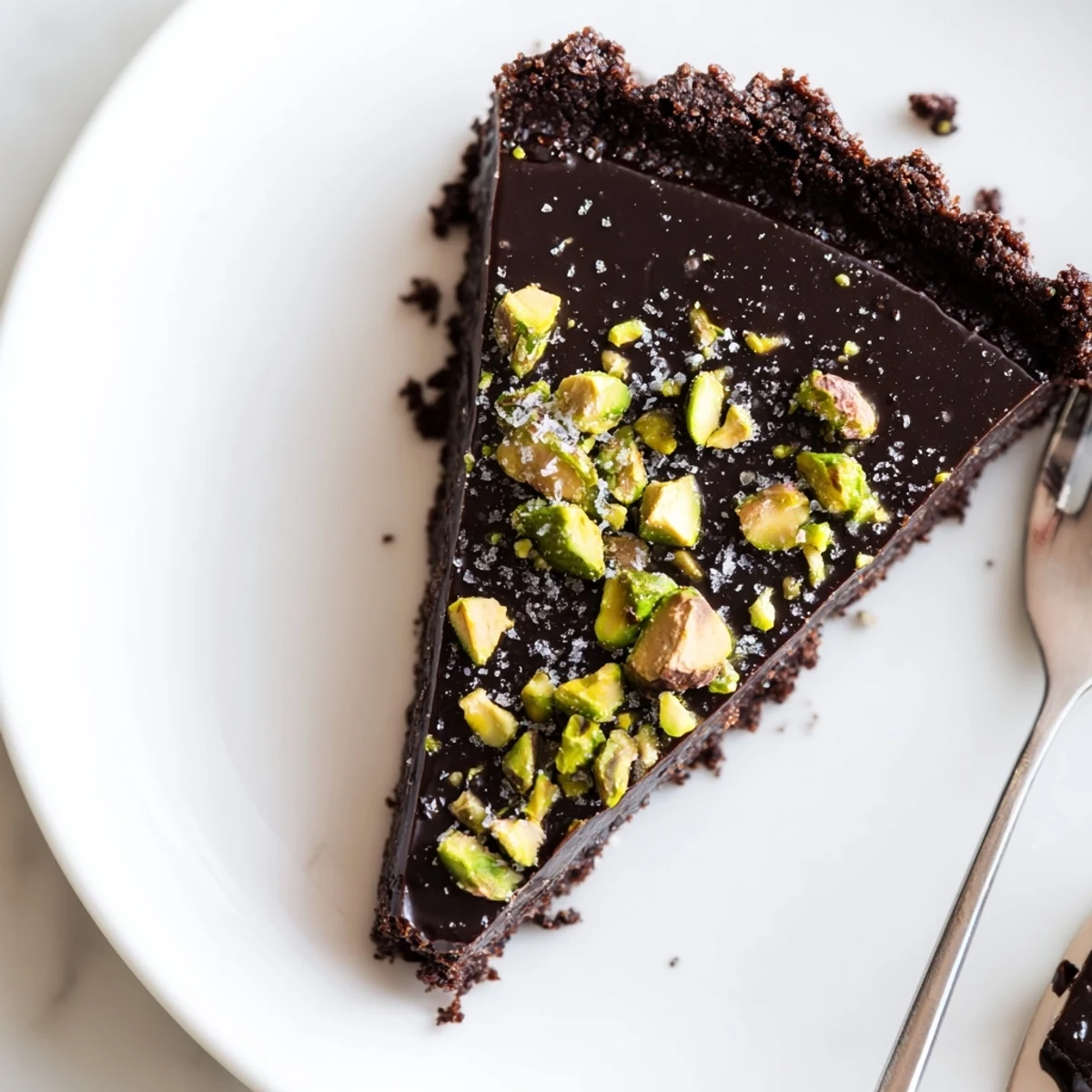 Silky Dark Chocolate Pistachio Tart sliced and served on a rustic white ceramic plate