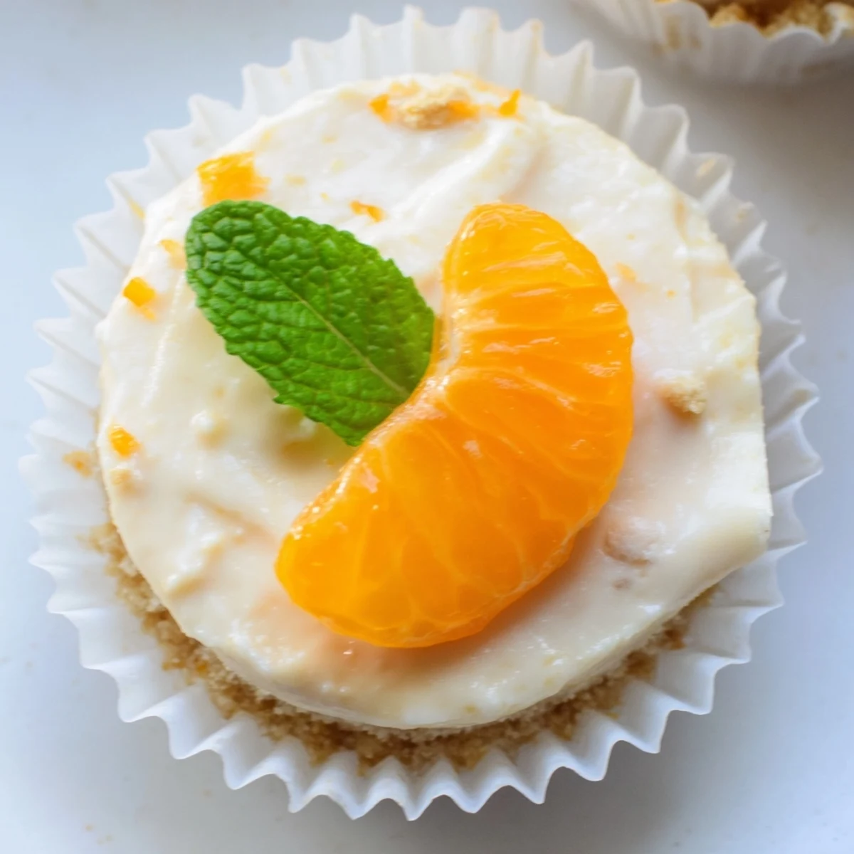 Creamy mini no bake orange cheesecakes topped with fresh orange segments and mint