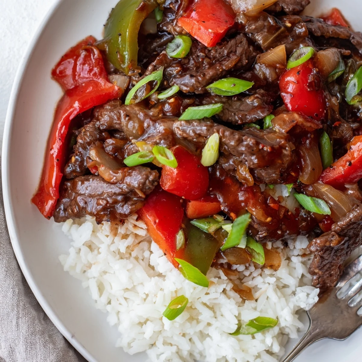 Juicy strips of Slow Cooker Pepper Steak served over fluffy white rice with green onions