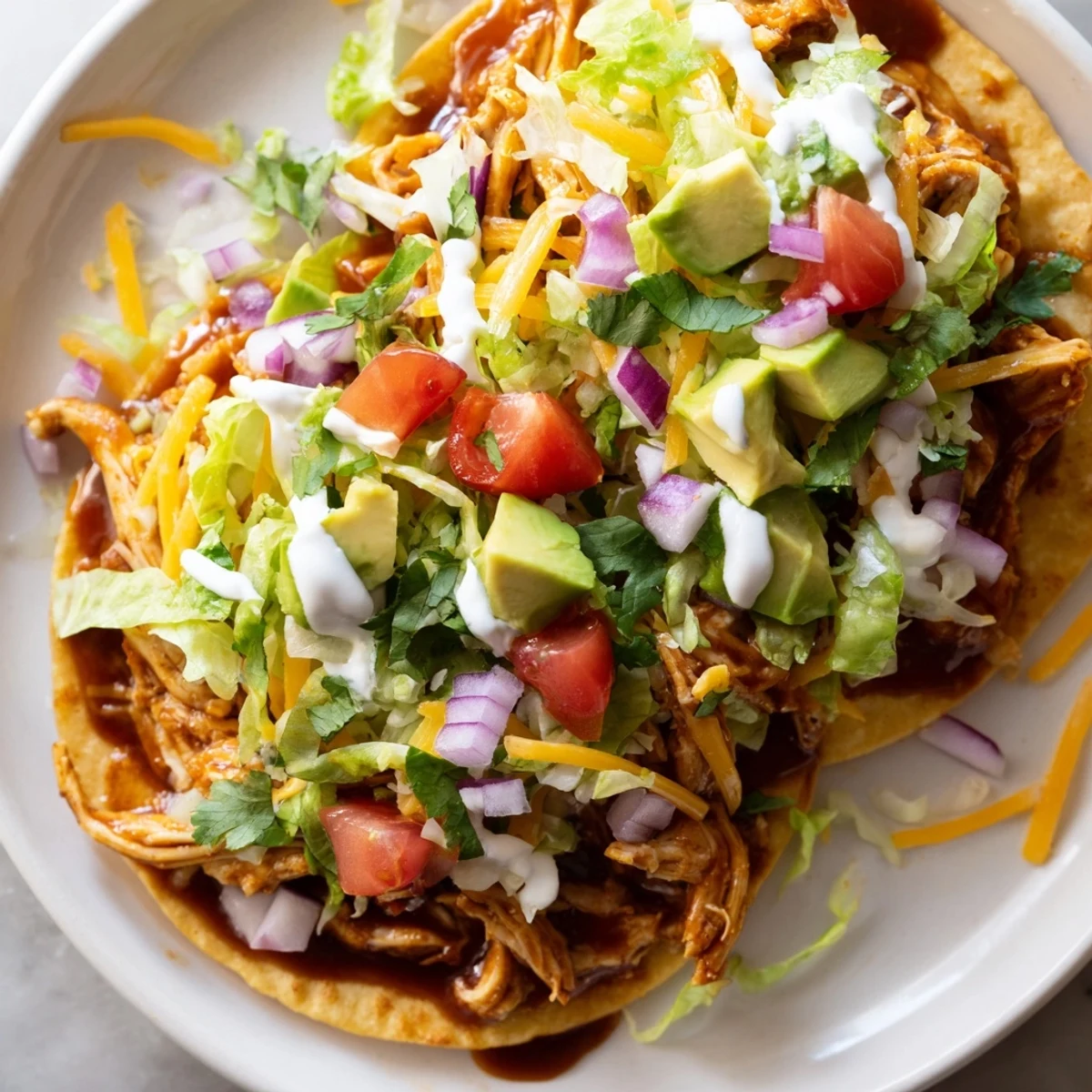 Crispy sweet smoky BBQ chicken tostadas loaded with melted cheese and fresh avocado slices