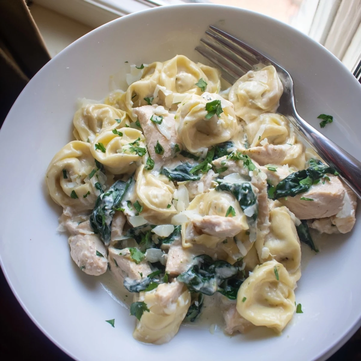 Creamy garlic chicken tortellini with spinach topped with grated Parmesan and fresh parsley