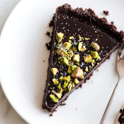 Silky Dark Chocolate Pistachio Tart sliced and served on a rustic white ceramic plate